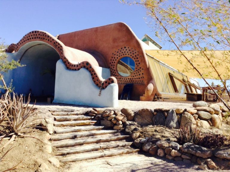 Sculpted Earthship with a wavy parapet, round bottle window and stone steps
