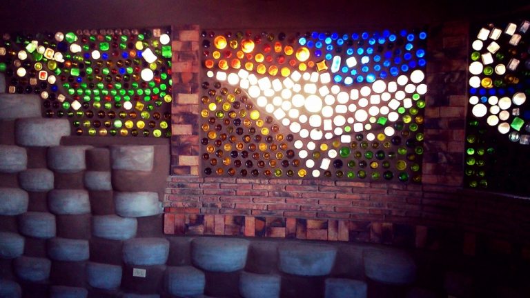 Colorful glass bottle wall glowing above a rammed-tire wall in a Rosarito Earthship