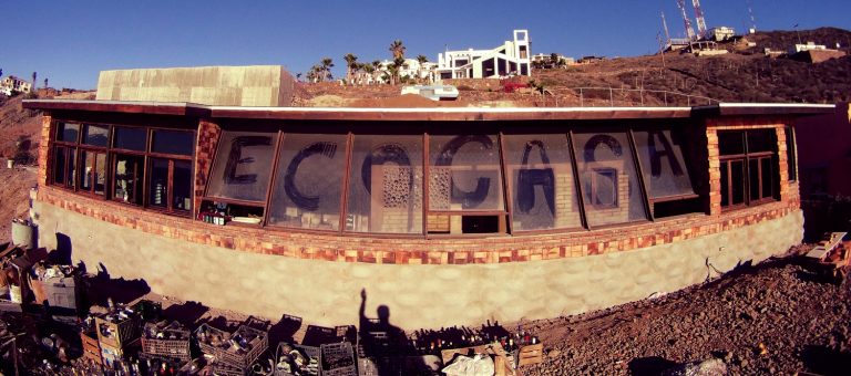 Panoramic view of an Earthship with a curved glazed front on a hillside