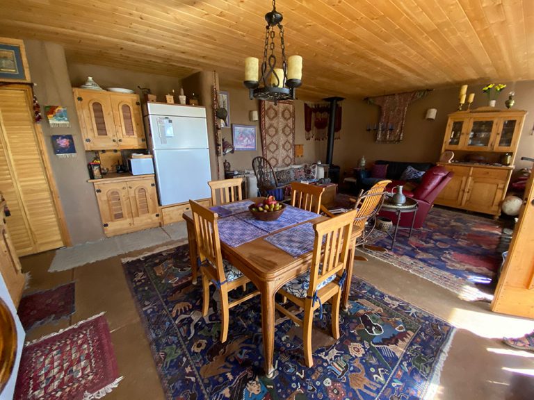 Dining and living room in a New Mexico Earthship with wood ceiling and rugs