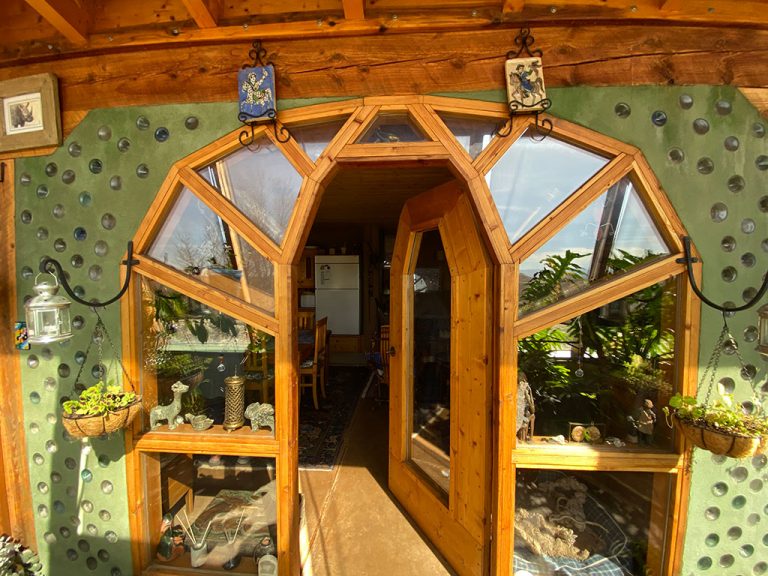 Arched timber-and-glass entry set in a bottle wall on a New Mexico Earthship