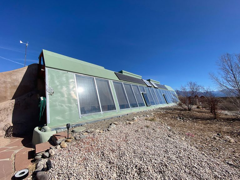 New Mexico Earthship on 3 acres with a south-facing glazed front under blue sky