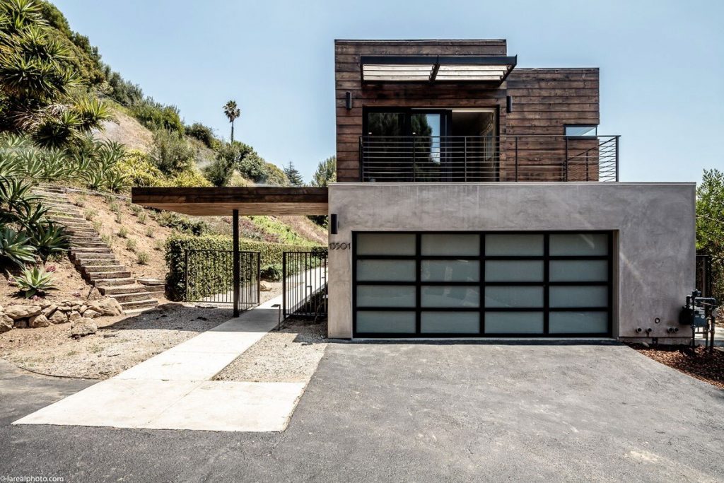 Bayliss Remodel: hillside home with wood-clad upper volume above a modern glass garage