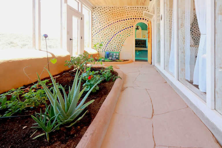 Greenhouse hallway with planter beds and a bottle-wall arch at the end
