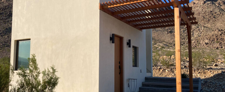 White plaster house with a timber pergola against the desert hills