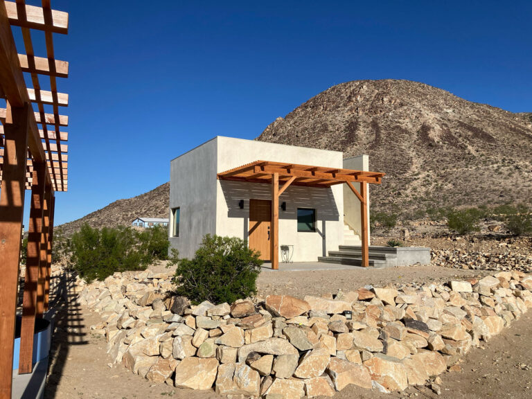 House and pergola behind a dry-stacked rock garden wall