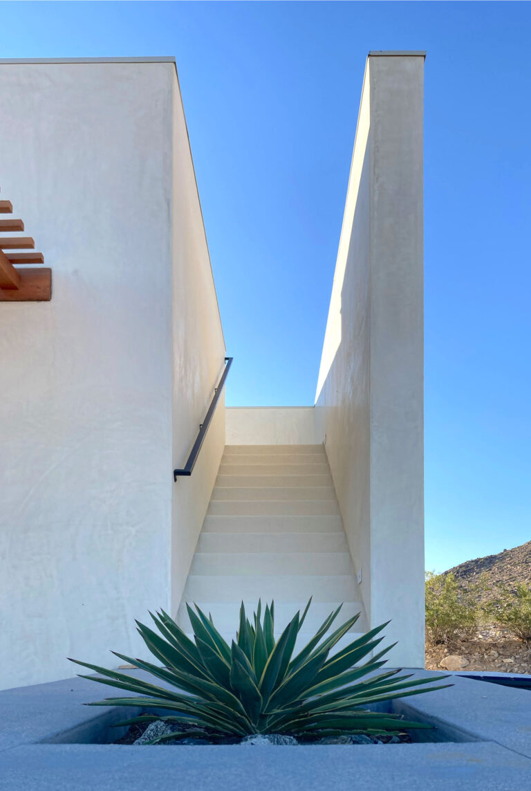Exterior stair between white plaster walls with an agave below