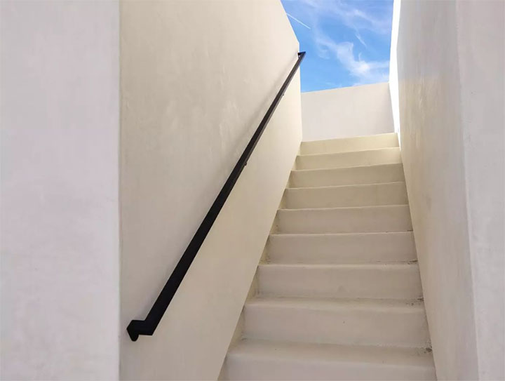 Plaster stair with a black steel handrail rising to the roof