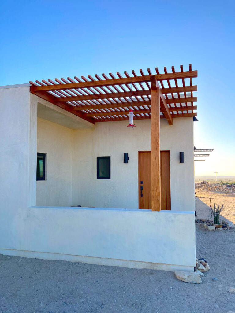Shaded porch under a timber pergola with a wood entry door