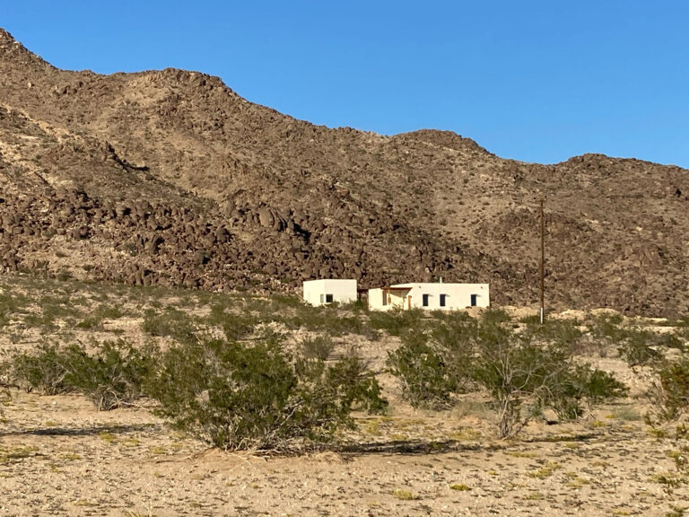The house seen from across the desert, low against the mountain